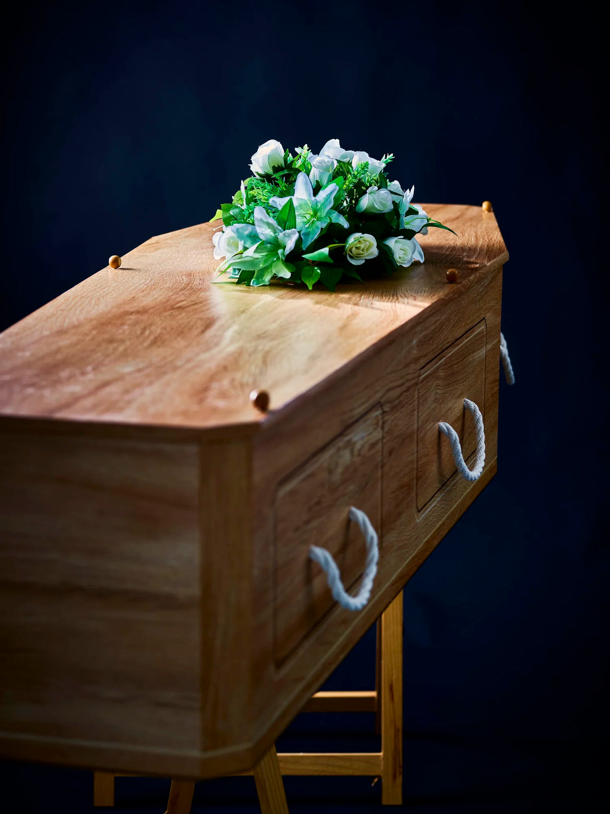 Premium Forest Board Coffin with white floral arrangement on dark backdrop